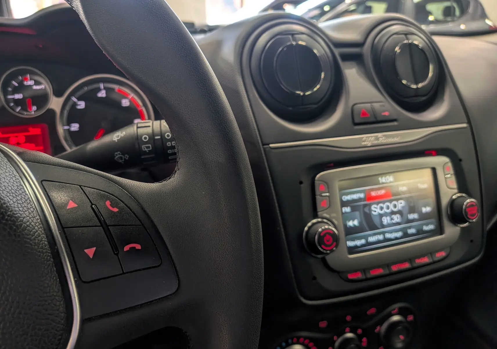 Intérieur de l'Alfa Romeo MiTo 2018 en vue rapprochée du tableau de bord avec volant et écran multimédia allumé.