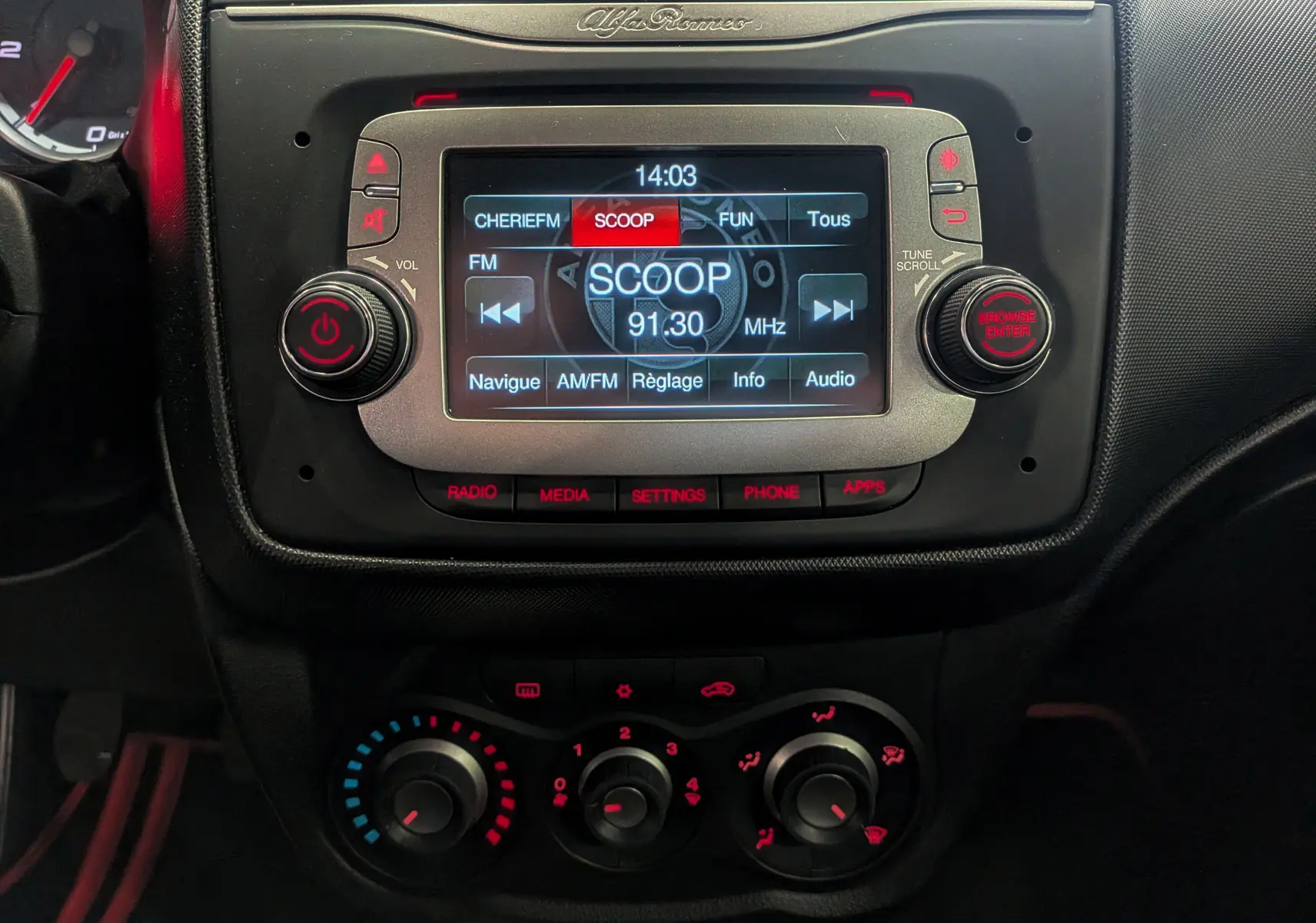 Gros plan sur la console centrale de l'Alfa Romeo MiTo rouge, affichant l'écran multimédia et les commandes de climatisation.