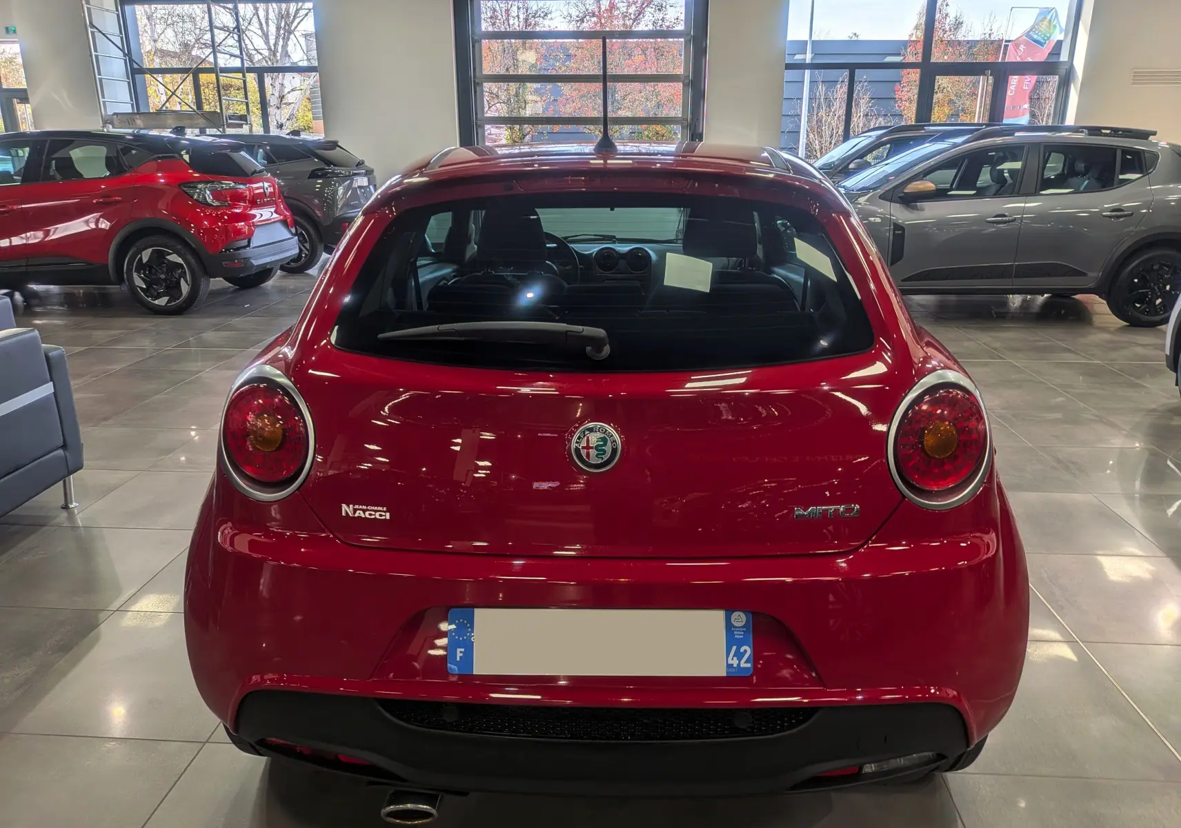 Vue arrière d'une Alfa Romeo MiTo rouge Alfa 2018 dans un showroom, avec logo et feux ronds caractéristiques.