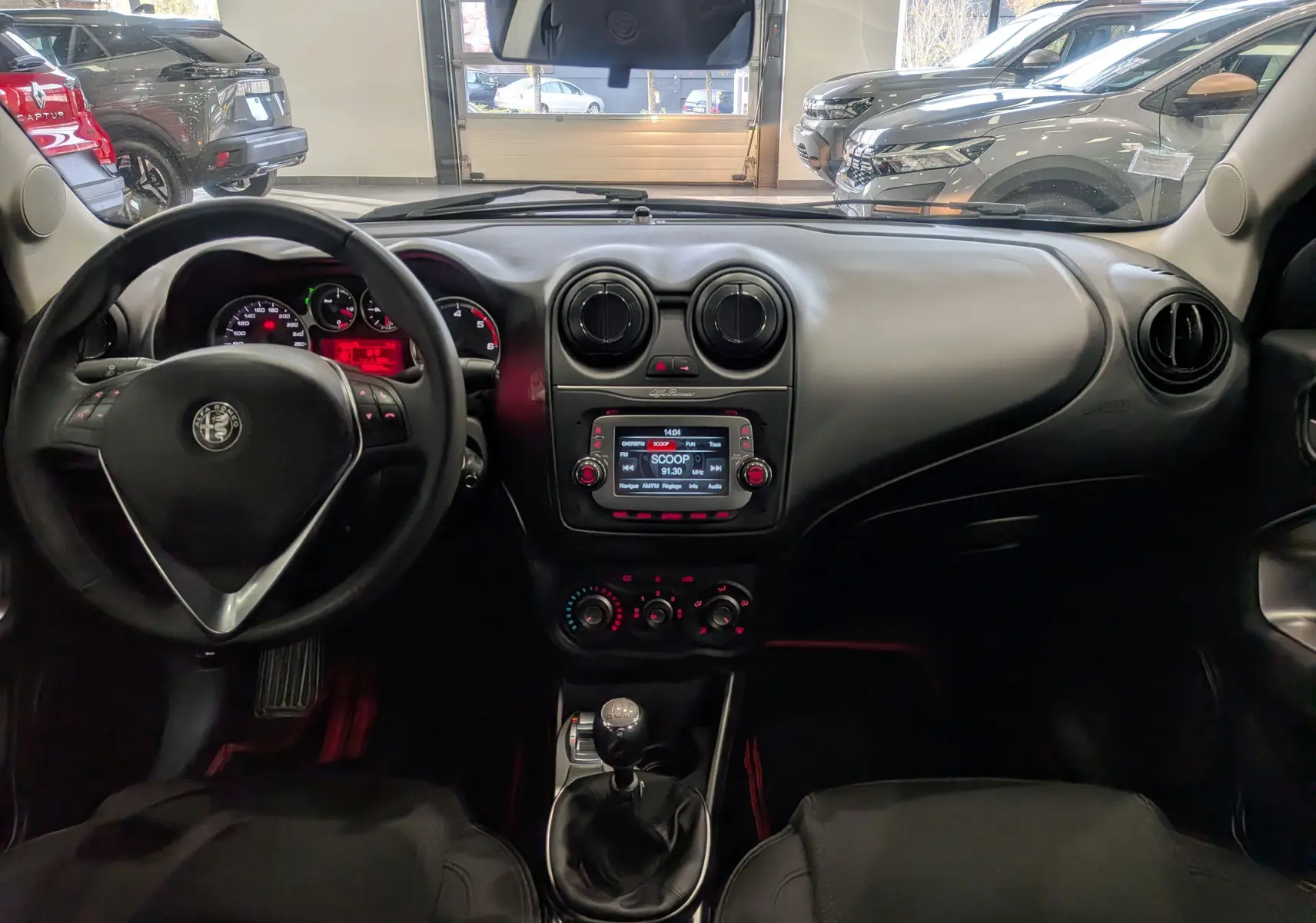 Vue intérieure frontale du tableau de bord noir de l'Alfa Romeo MiTo 1.3 JTDm avec volant et levier de vitesses manuelle.