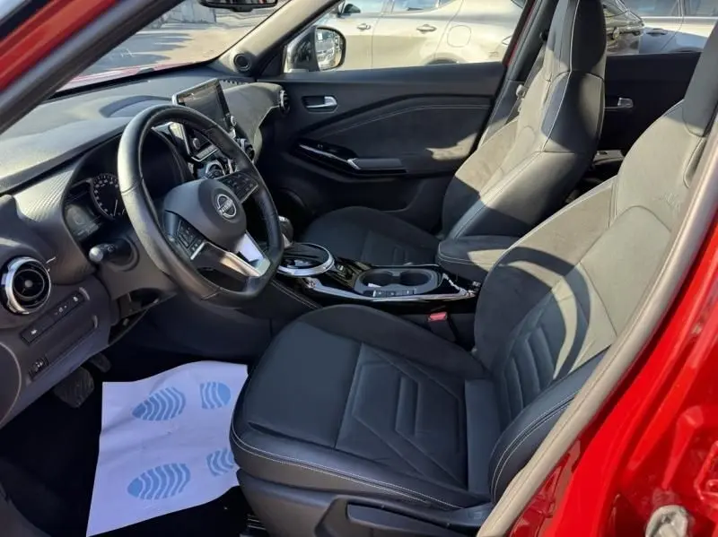 Intérieur avant du Nissan Juke 1.6 Hybrid rouge Fuji, sièges noirs et tableau de bord avec volant multifonction.