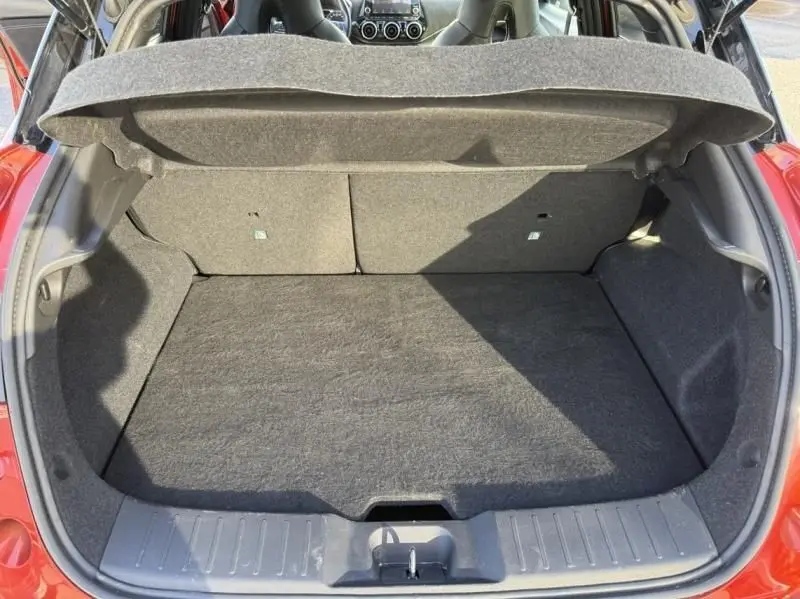 Vue arrière du coffre ouvert du Nissan Juke 1.6 Hybrid rouge Fuji avec intérieur de coffre gris foncé.