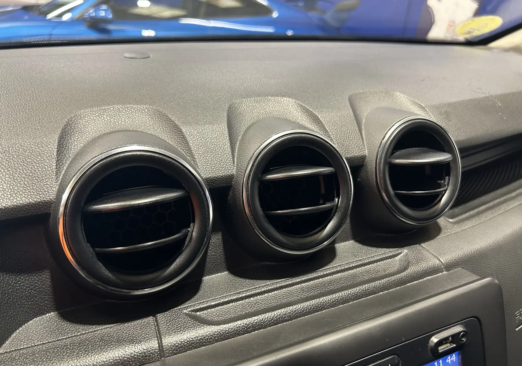 Gros plan sur les trois aérateurs ronds du tableau de bord d’un Dacia Duster noir, intérieur en plastique texturé.