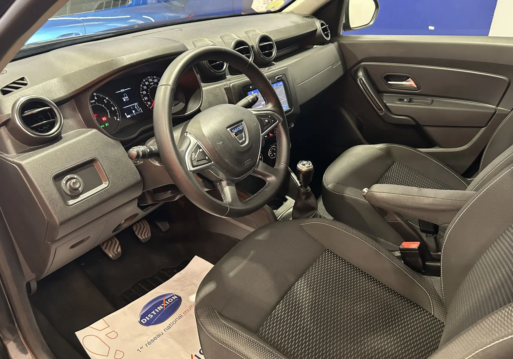 Vue intérieure côté conducteur du Dacia Duster noir 2018, montrant le volant, la console centrale et les sièges en tissu.