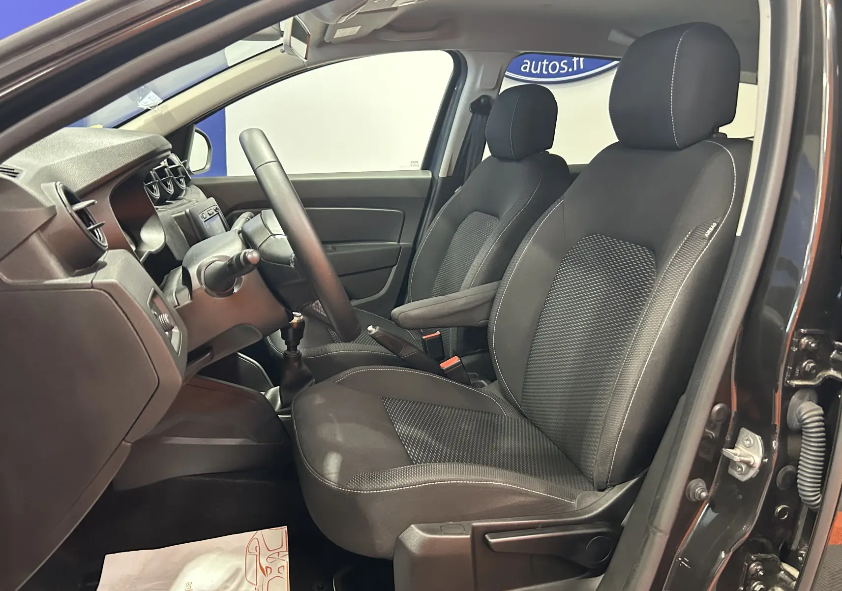 Vue intérieure côté conducteur du Dacia Duster noir 2018, mettant en valeur les sièges en tissu et le tableau de bord simple.