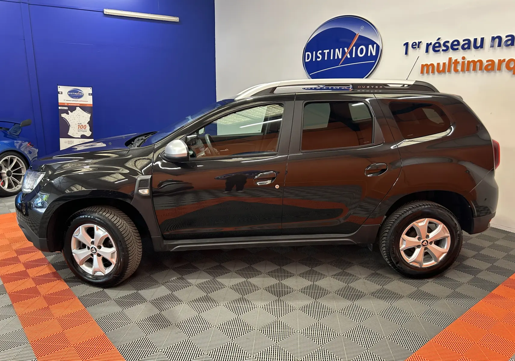 Vue de profil côté gauche d'un Dacia Duster noir 2018 avec jantes alliage et barres de toit argentées en showroom.