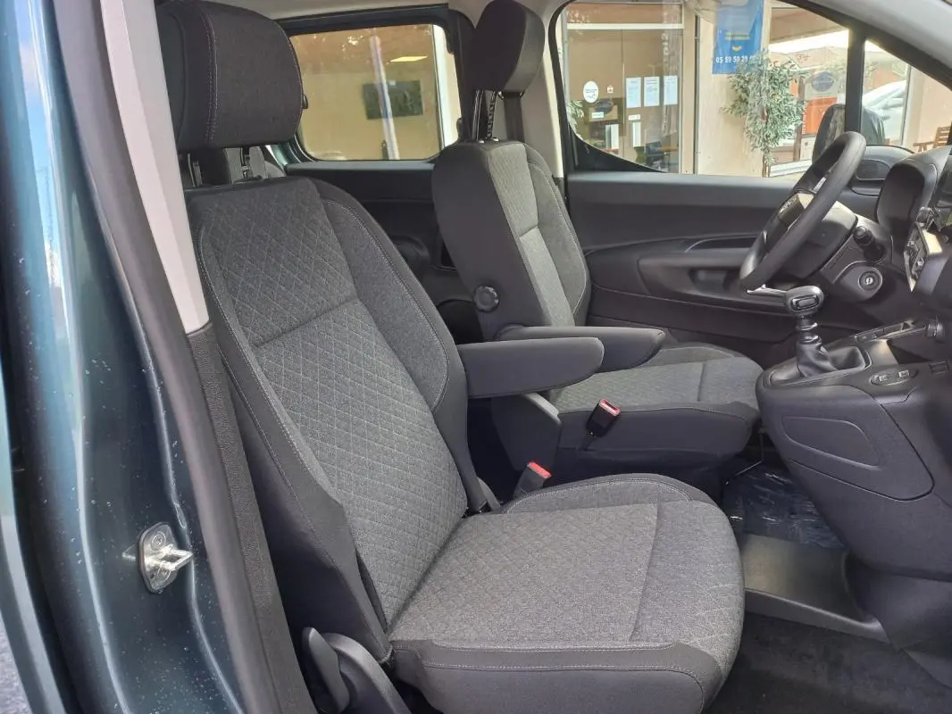 Vue intérieure côté conducteur de l'Opel Combo Life M 2025 bleu, montrant les sièges avant en tissu gris et la boîte manuelle.