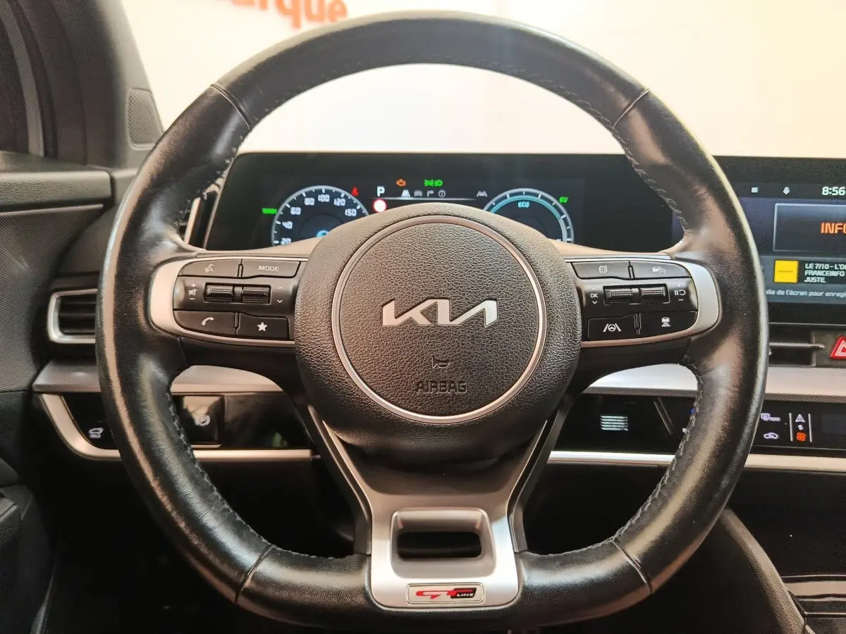 Volant cuir noir avec logo KIA et badge GT-Line, tableau de bord digital lumineux du Kia Sportage gris clair 2022.