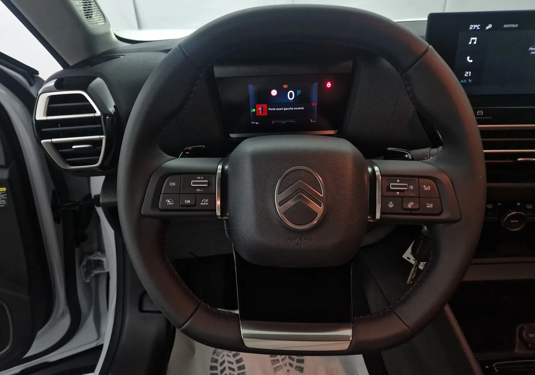 Vue rapprochée du volant cuir noir du Citroën C4 blanc Okenite 2025 avec commandes intégrées et tableau de bord numérique.