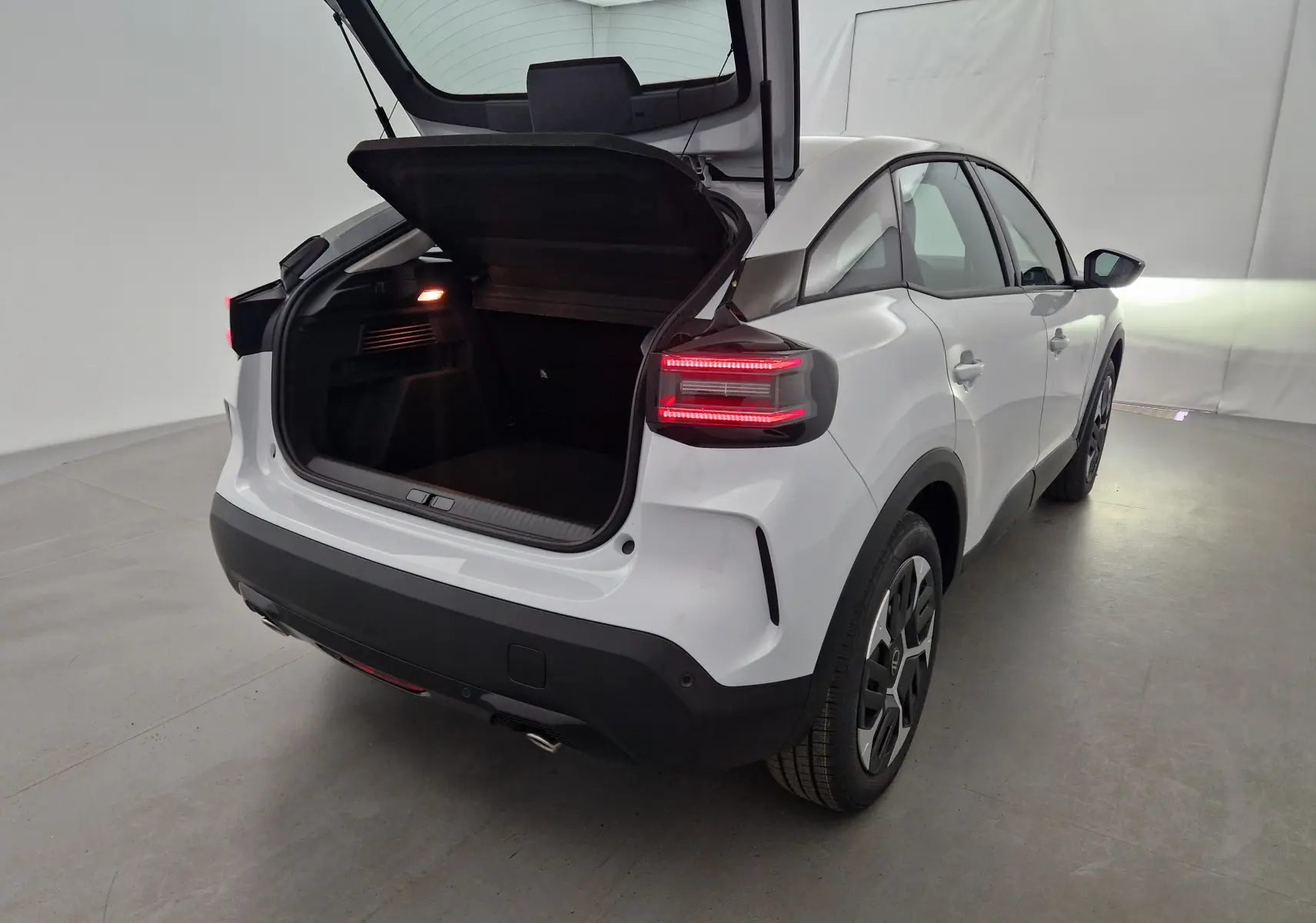 Vue arrière droite d'une Citroën C4 blanc Okenite 2025 avec coffre ouvert et feux arrière allumés dans un studio.