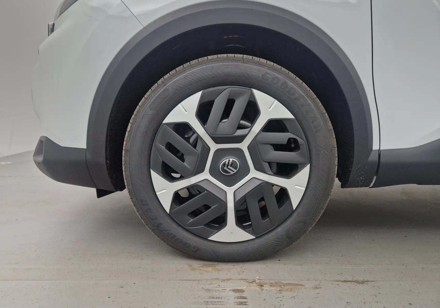 Gros plan sur la roue avant gauche d'une Citroën C4 blanche Okenite 2025 avec jante au design géométrique noir et argent.