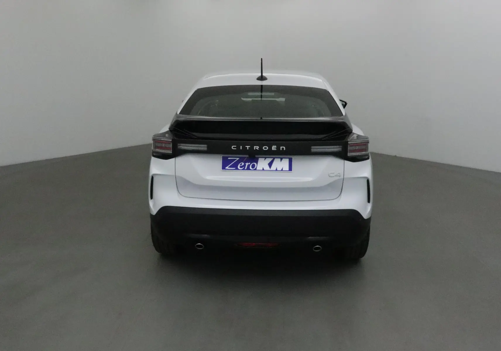 Vue arrière d'une Citroën C4 blanche Okenite avec bande noire et feux arrière horizontaux dans un studio.