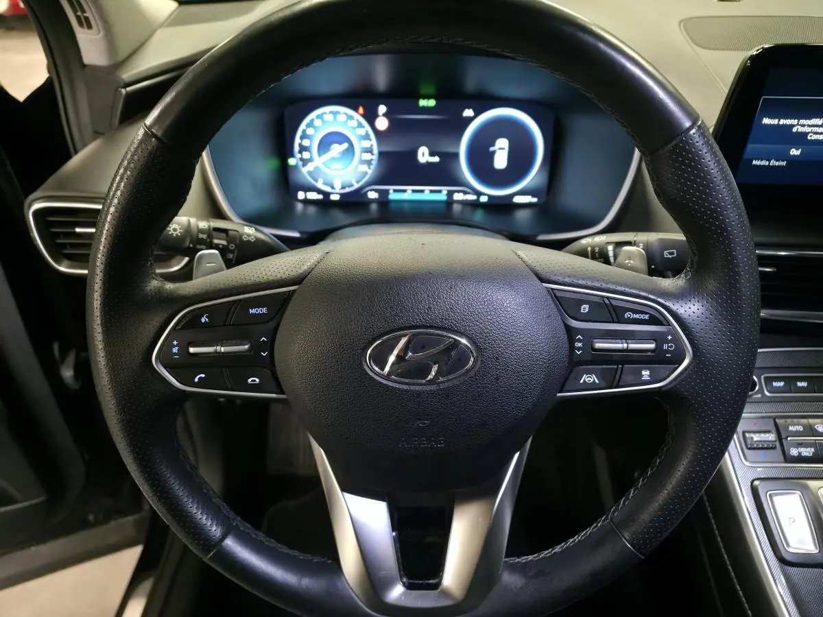 Vue rapprochée du volant cuir perforé noir et du tableau de bord numérique du Hyundai Santa Fé 2023 hybride rechargeable.