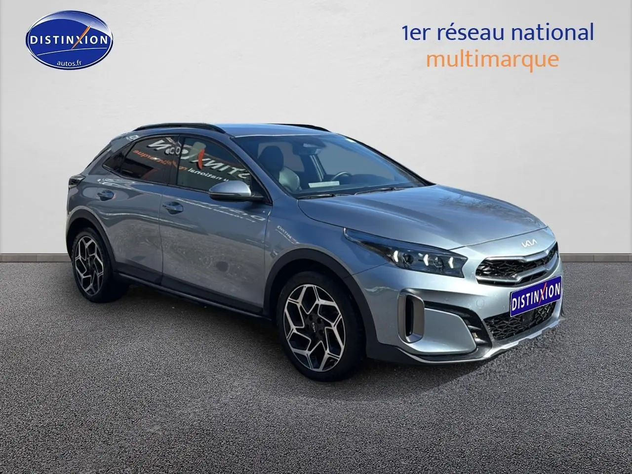 KIA Xceed gris en 3/4 avant droit, avec jantes alu et calandre chromée visible sur fond neutre.