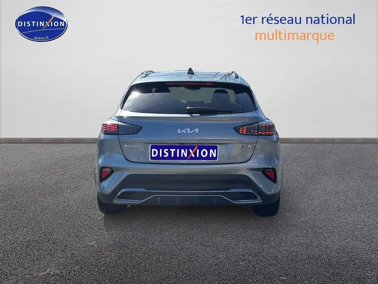 Vue arrière d'un KIA Xceed gris 2024 avec feux arrière LED et becquet intégré sur un sol bitumé.
