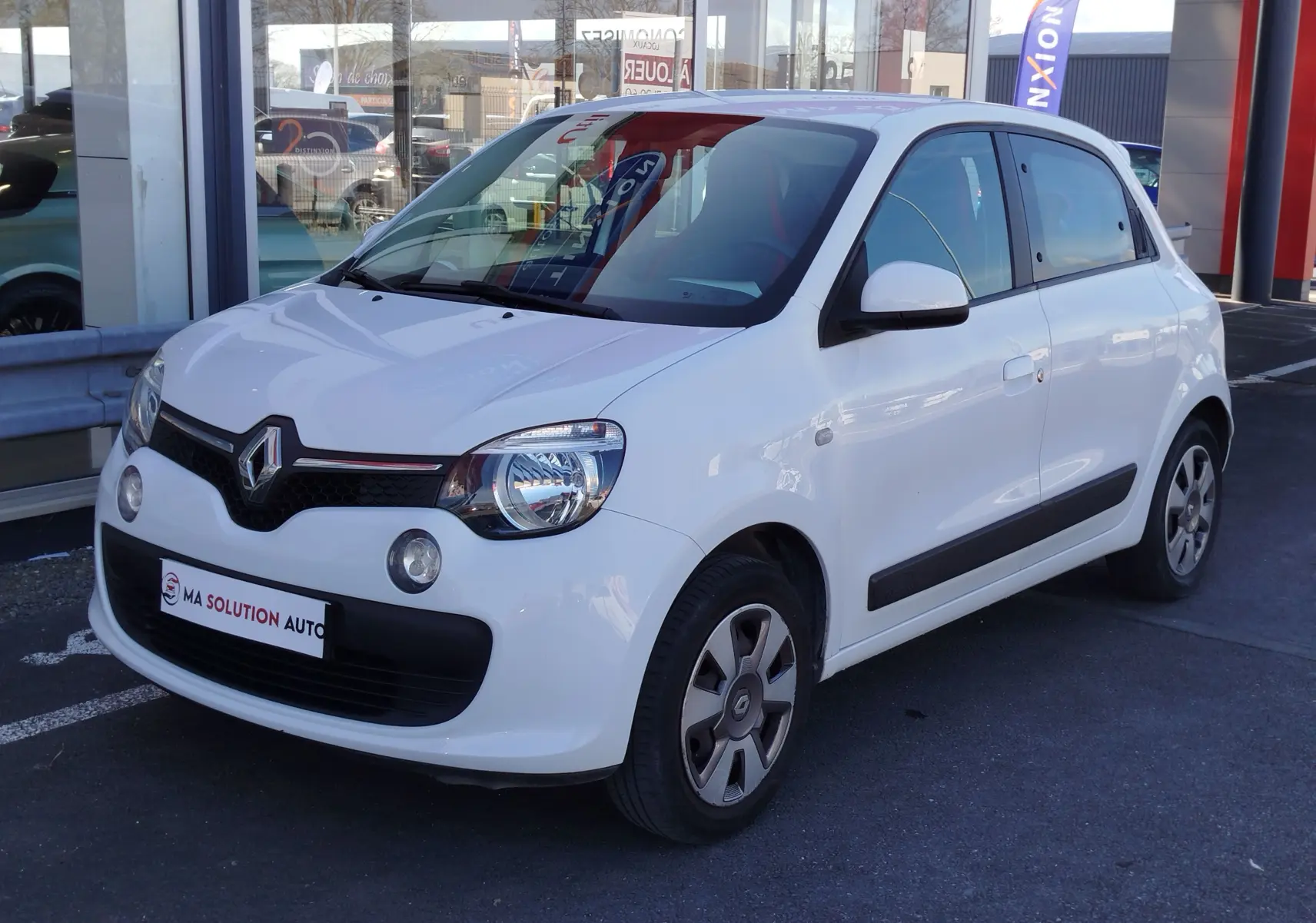 Renault Twingo blanc cristal vue 3/4 avant droit, compacte avec phares ronds et bandeau noir frontal.