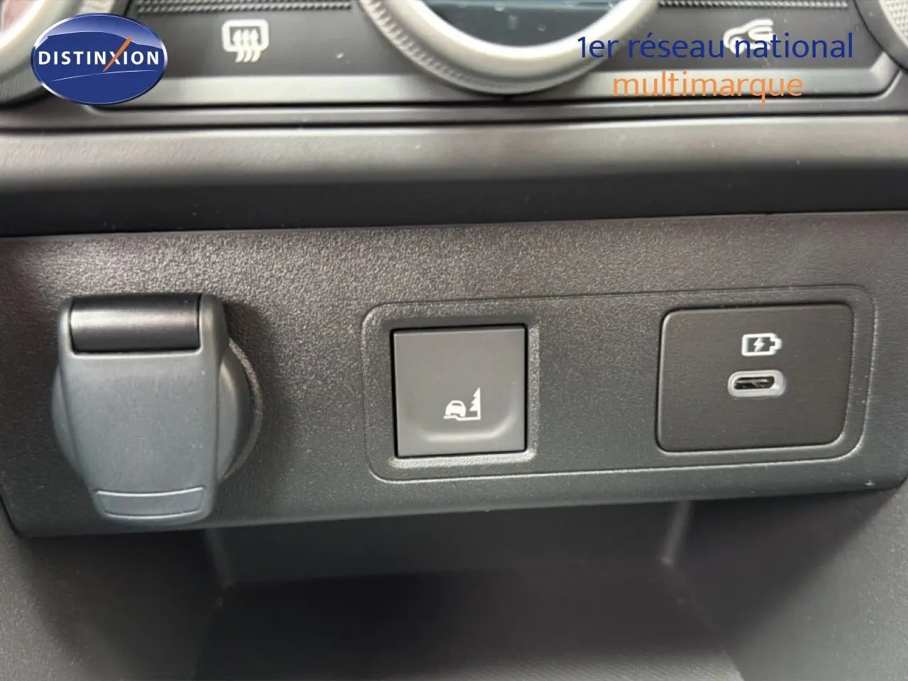 Détail intérieur montrant une prise 12V, un bouton d'assistance en côte et un port USB-C sur tableau de bord noir.