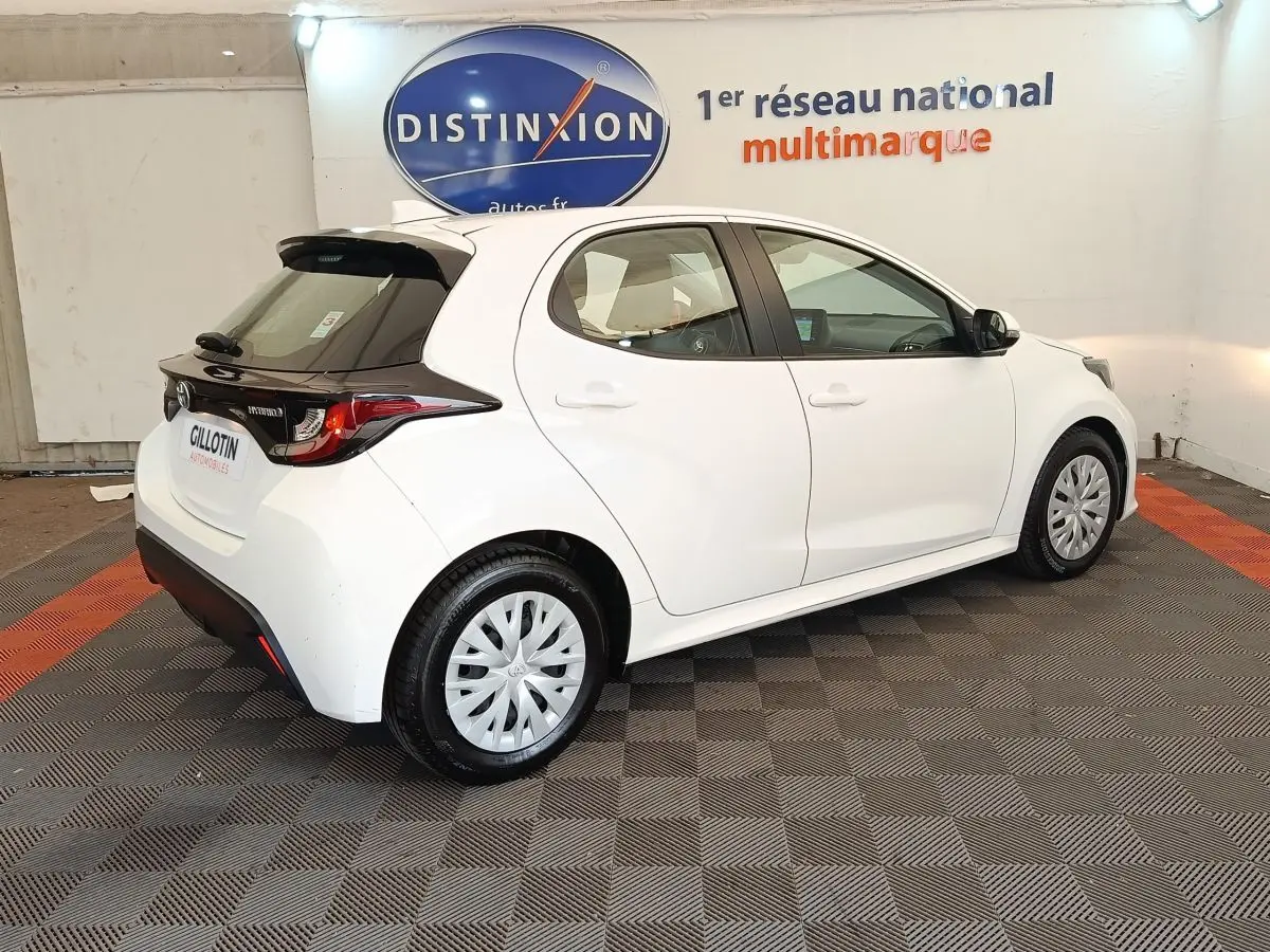 Toyota Yaris hybride blanche vue en 3/4 arrière droit, avec toit noir et jantes à enjoliveurs.