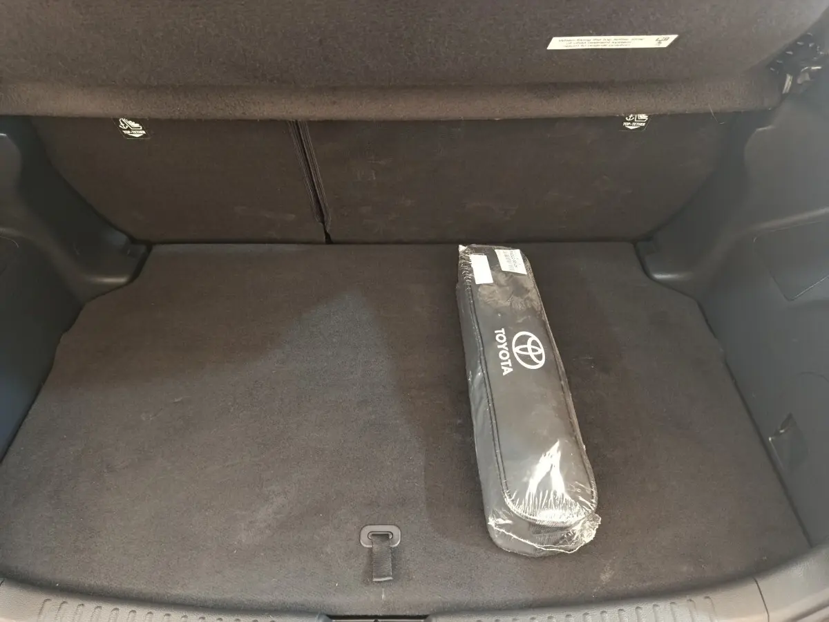 Coffre arrière de Toyota Yaris hybride blanche 2022, vue intérieure montrant la banquette rabattue et une housse Toyota.