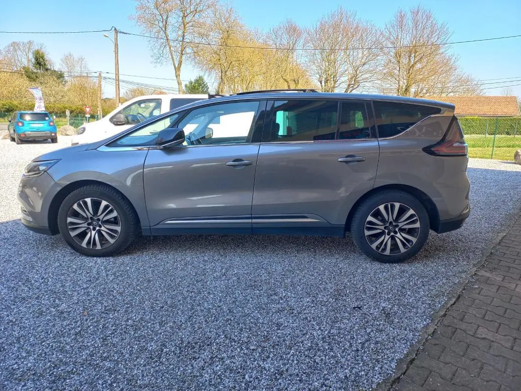 Vue de profil côté gauche d'un Renault Espace gris 2017 garé sur un sol gravillonné, avec jantes alliage et vitres teintées.