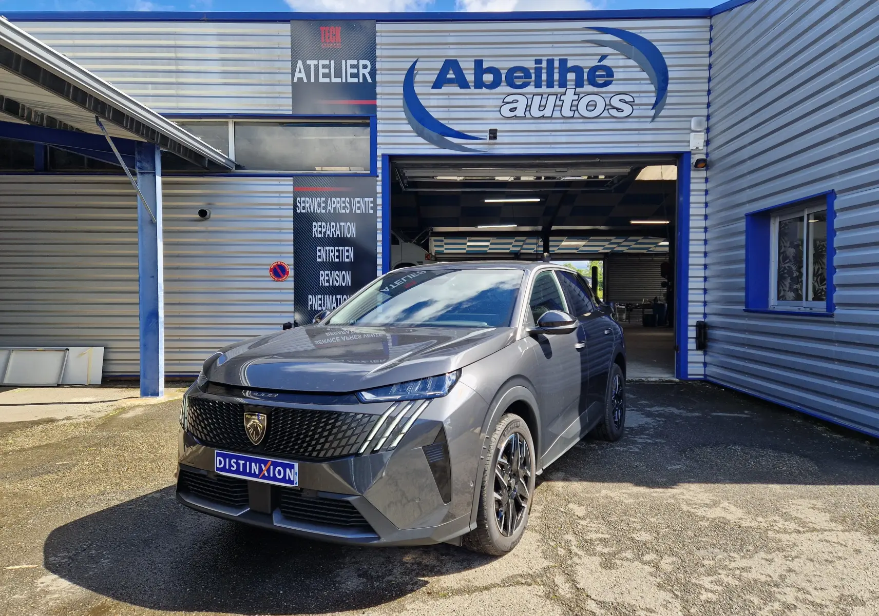 Peugeot 3008 gris titane en 3/4 avant droit devant un garage avec logo Abeilhé autos visible.