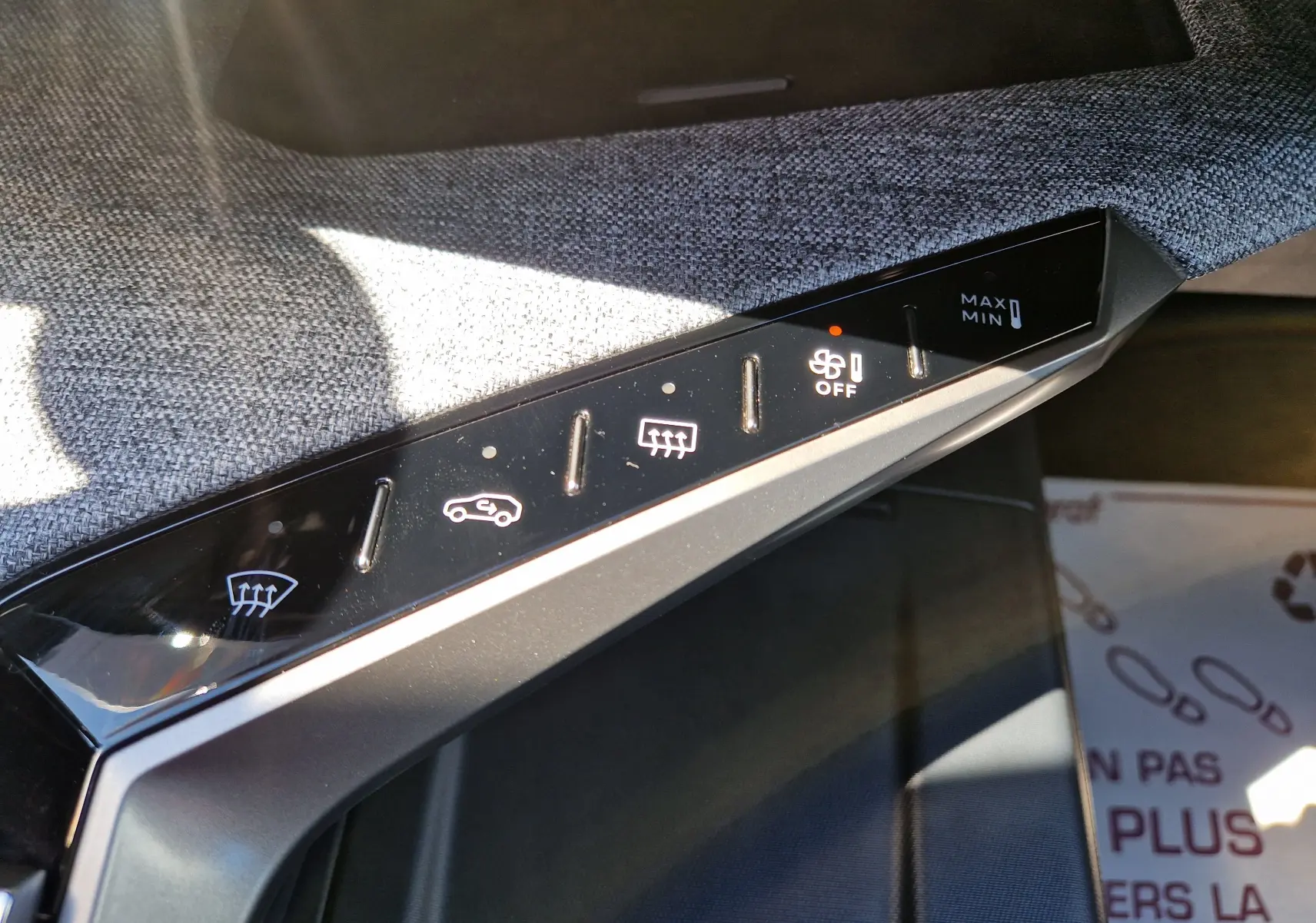 Gros plan sur les commandes de climatisation du Peugeot 3008 gris titane, avec boutons tactiles rétroéclairés et tissu gris en arrière-plan.