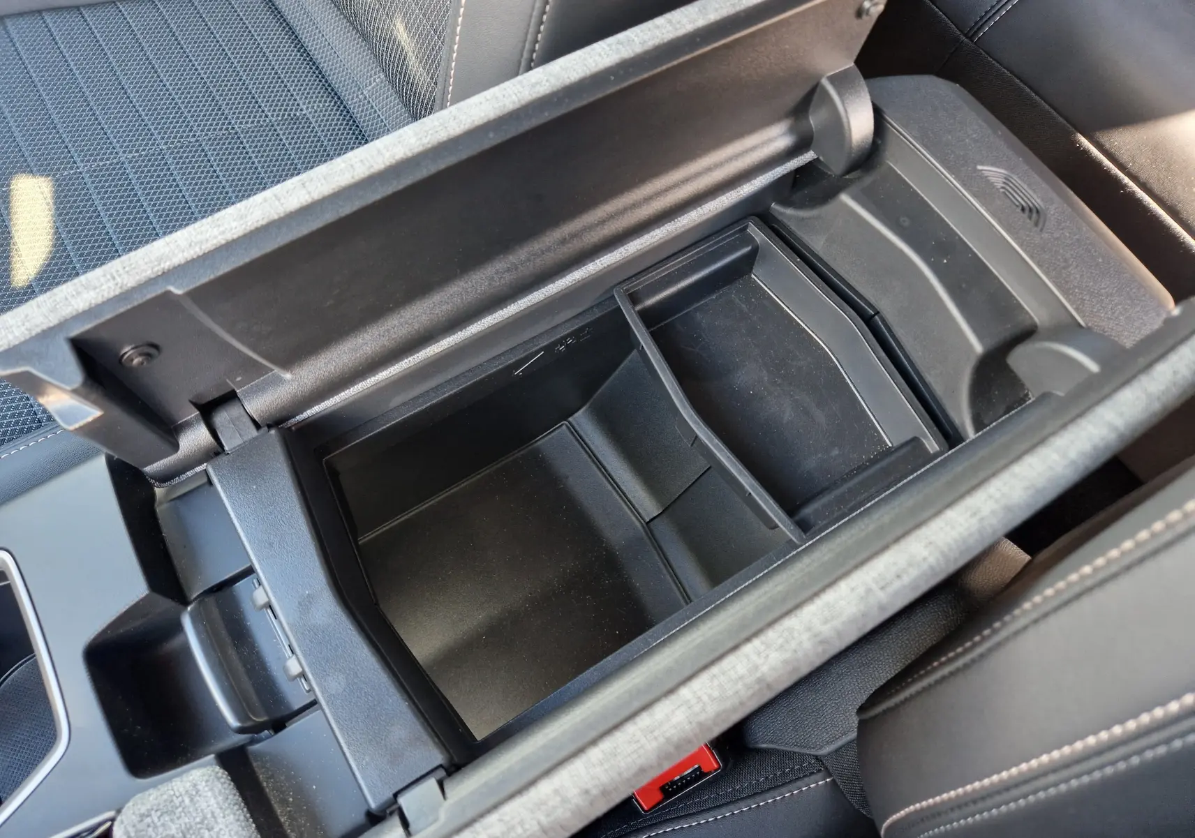 Vue plongeante sur le rangement central ouvert du Peugeot 3008 1.2 HYBRID 145 gris titane, intérieur noir avec surpiqûres claires.
