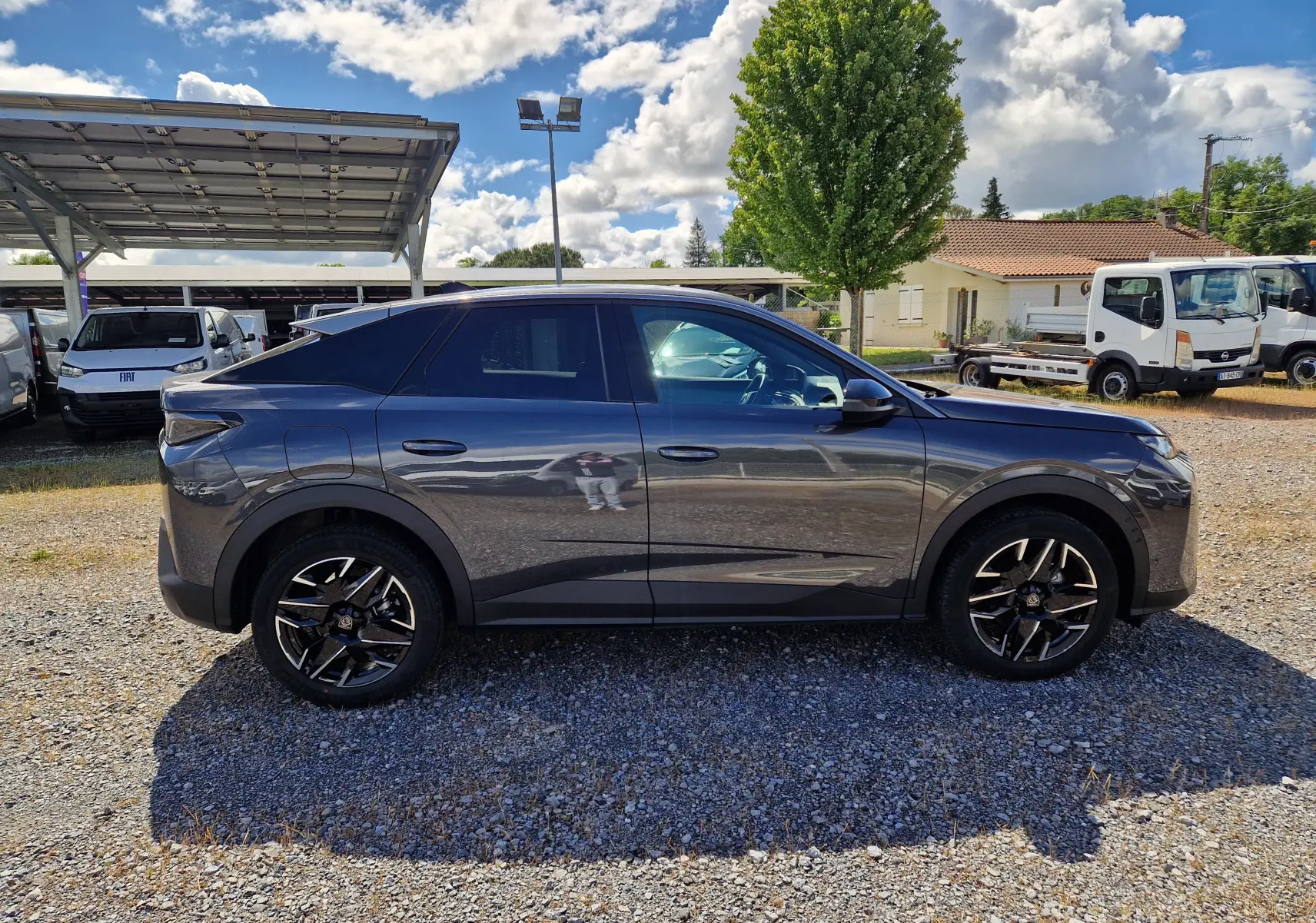 Peugeot 3008 1.2 Hybrid 145 Allure gris titane vue de profil côté gauche sur un sol gravillonné.