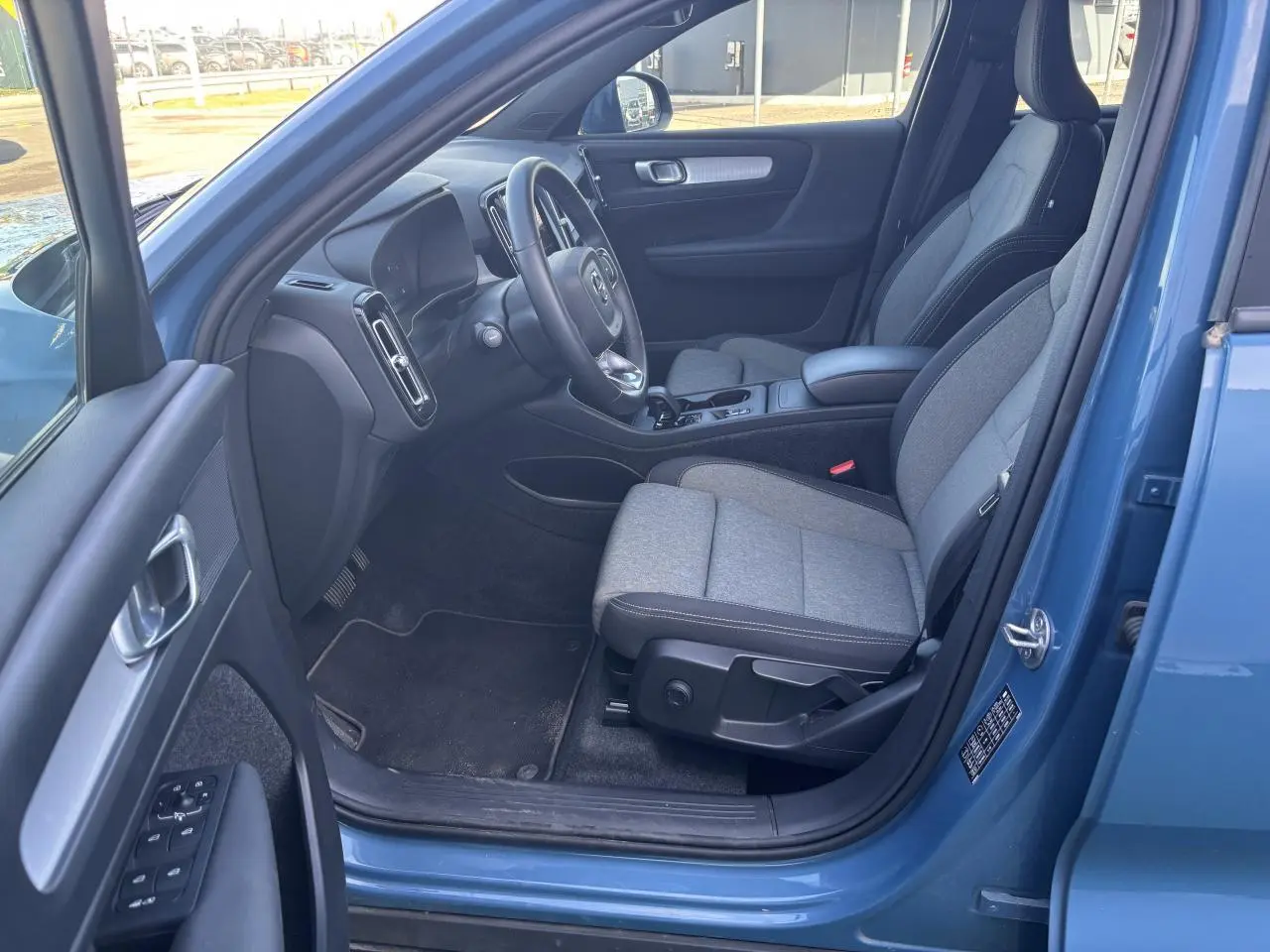 Intérieur avant côté conducteur du Volvo XC40 Fjord Blue 2024 avec sièges gris et tableau de bord moderne.