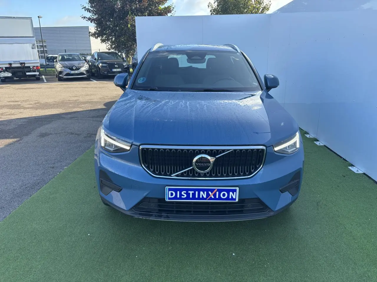 Vue frontale du Volvo XC40 Fjord Blue Metal 2024 avec calandre noire et logo centré sur fond vert.