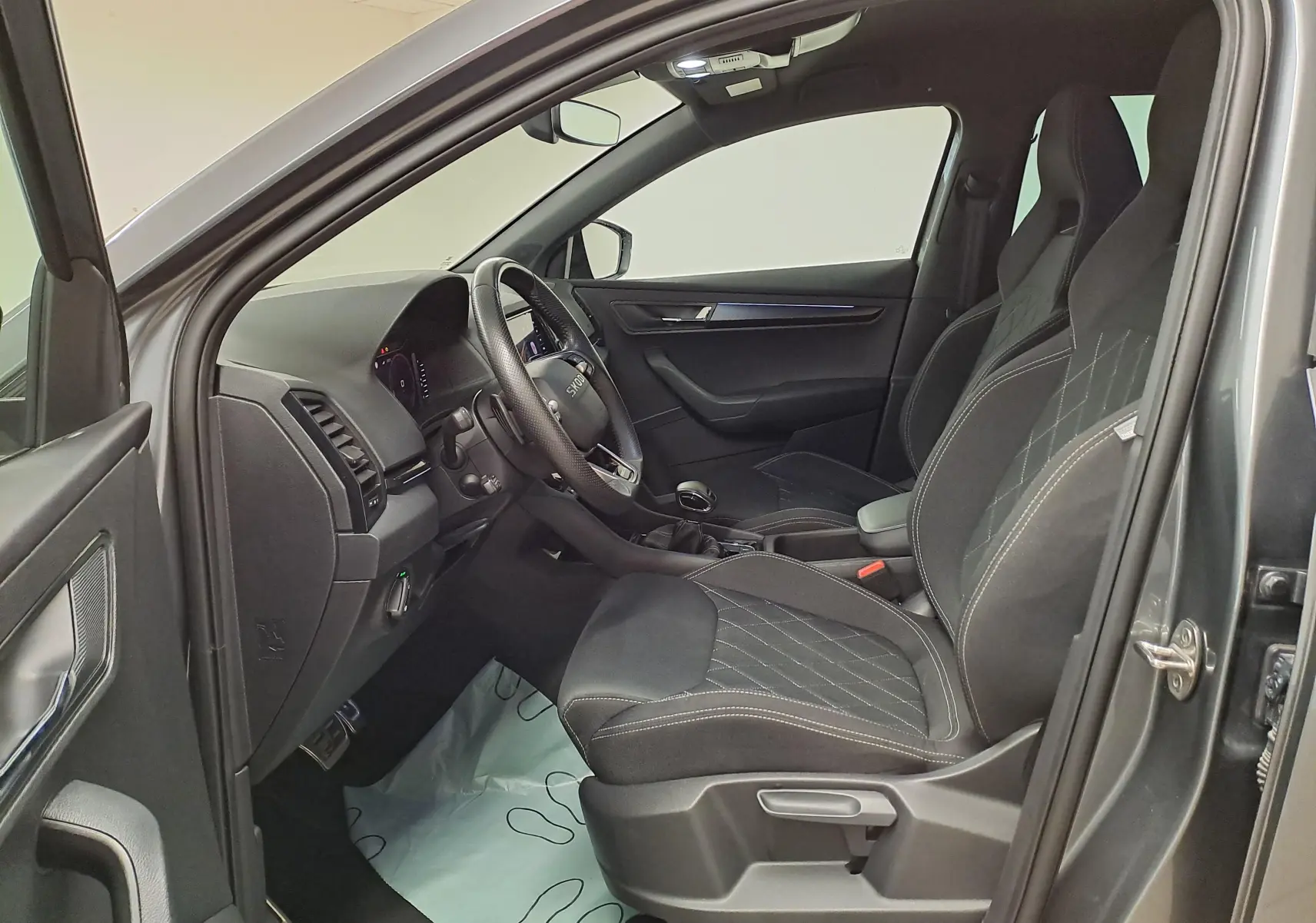 Vue intérieure côté conducteur du Skoda Karoq gris graphite 2025, mettant en valeur les sièges sport et le tableau de bord moderne.