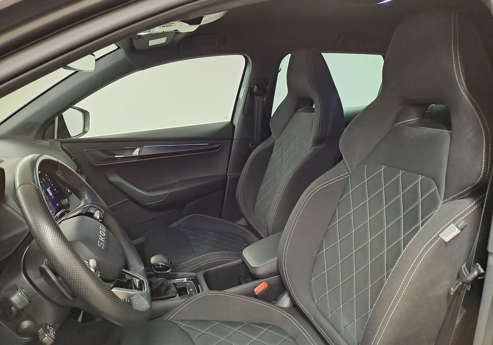 Vue intérieure côté conducteur du Skoda Karoq 2.0 TDI 150 DSG7 Sportline avec sièges noirs à surpiqûres croisées.