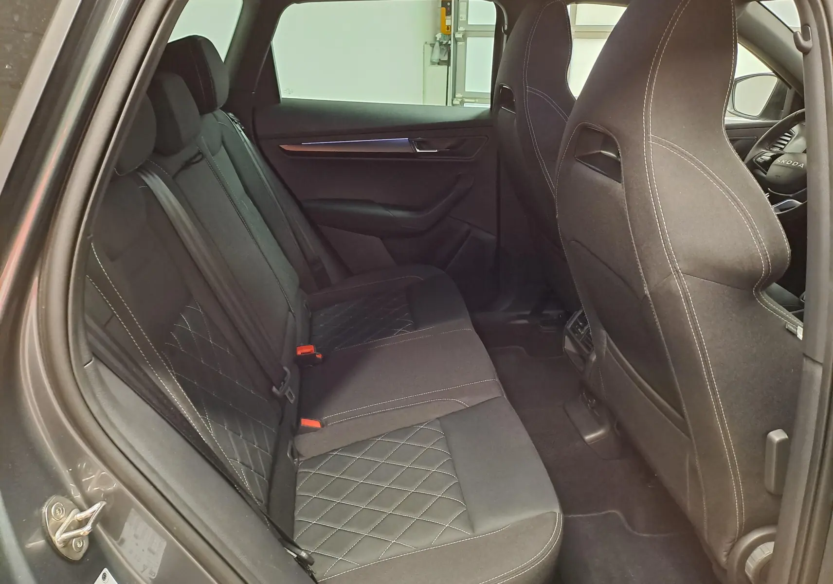 Vue intérieure côté gauche des sièges arrière noirs avec surpiqûres blanches du Skoda Karoq 2025 gris graphite Sportline.