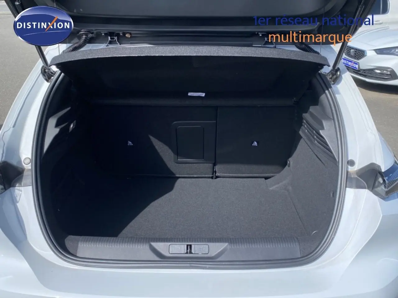 Coffre ouvert vu de l'arrière d'une Peugeot 308 Hybrid blanche, montrant un espace de chargement vide et propre.