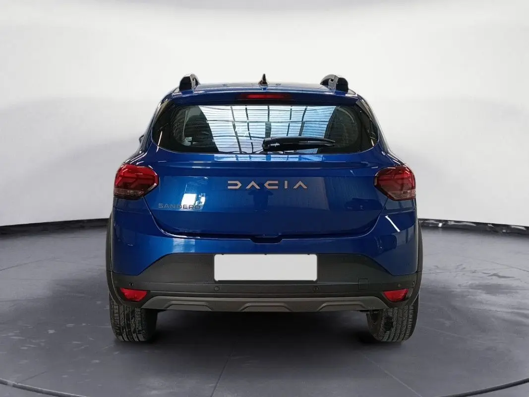 Vue arrière d'une Dacia Sandero Stepway 2025 en bleu Iron, avec feux arrière rouges et toit équipé de barres de toit.