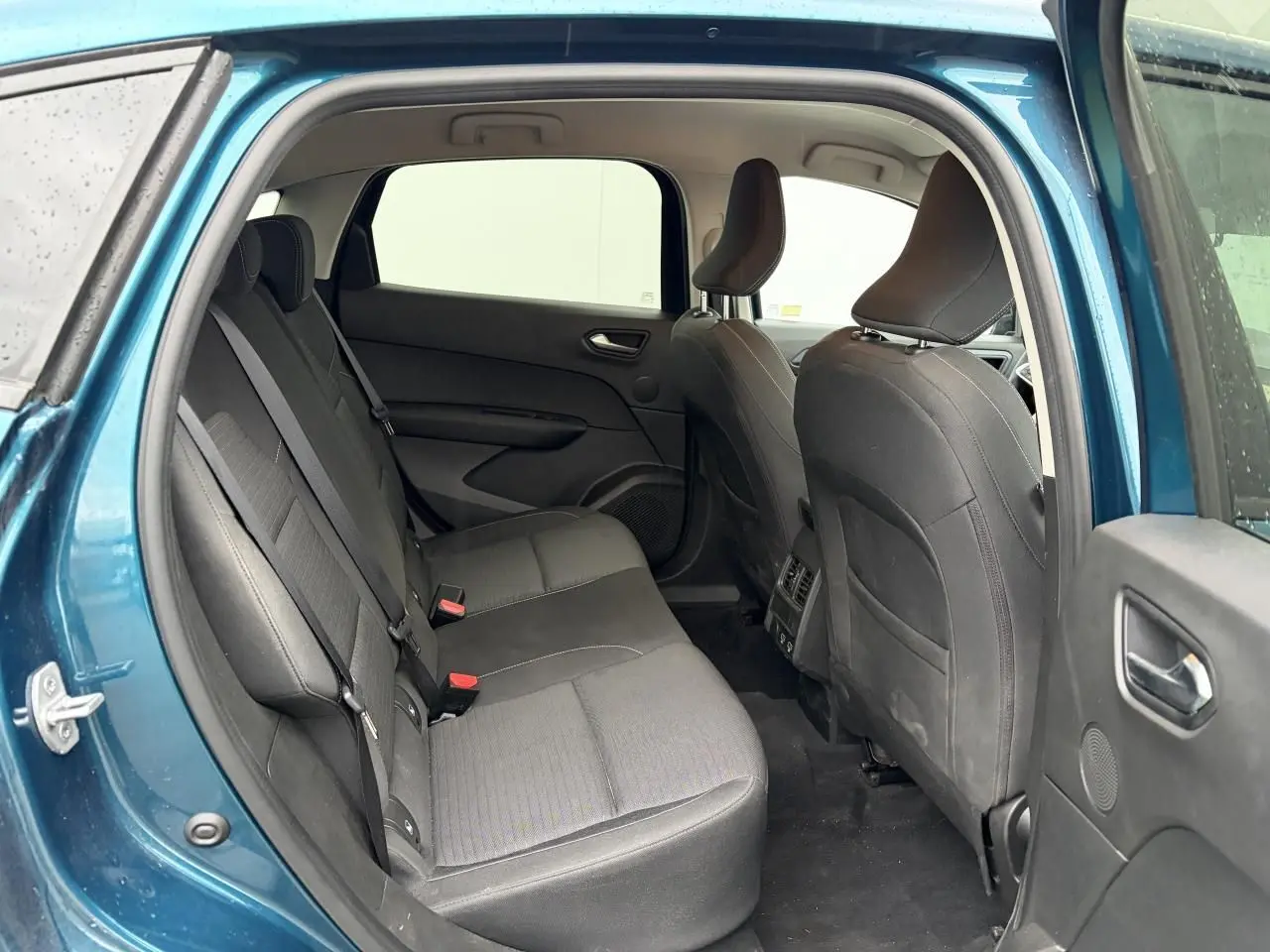 Vue intérieure arrière du Renault Arkana bleu Zanzibar, montrant les sièges arrière en tissu gris et les portières ouvertes.