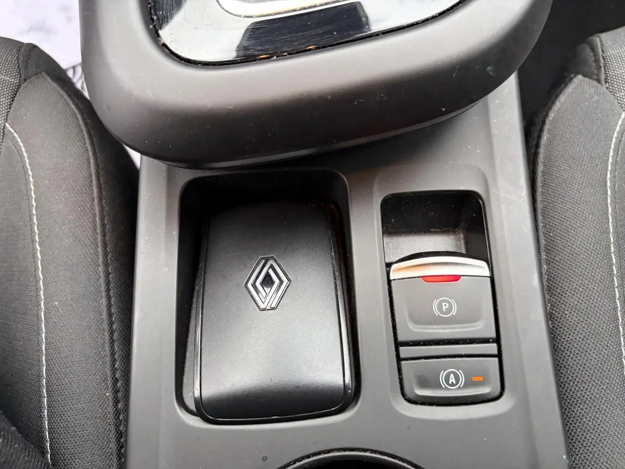 Gros plan sur la console centrale noire avec logo Renault et commandes de frein de parking et auto-hold du Renault Arkana.
