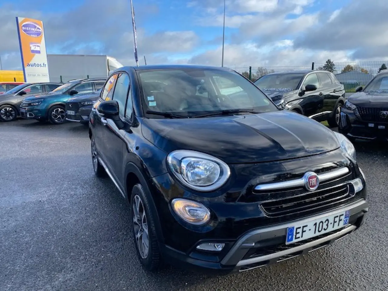 Vue 3/4 avant d'un FIAT 500X Cross noir 2016 avec calandre chromée et feux ronds allumés sur parking.