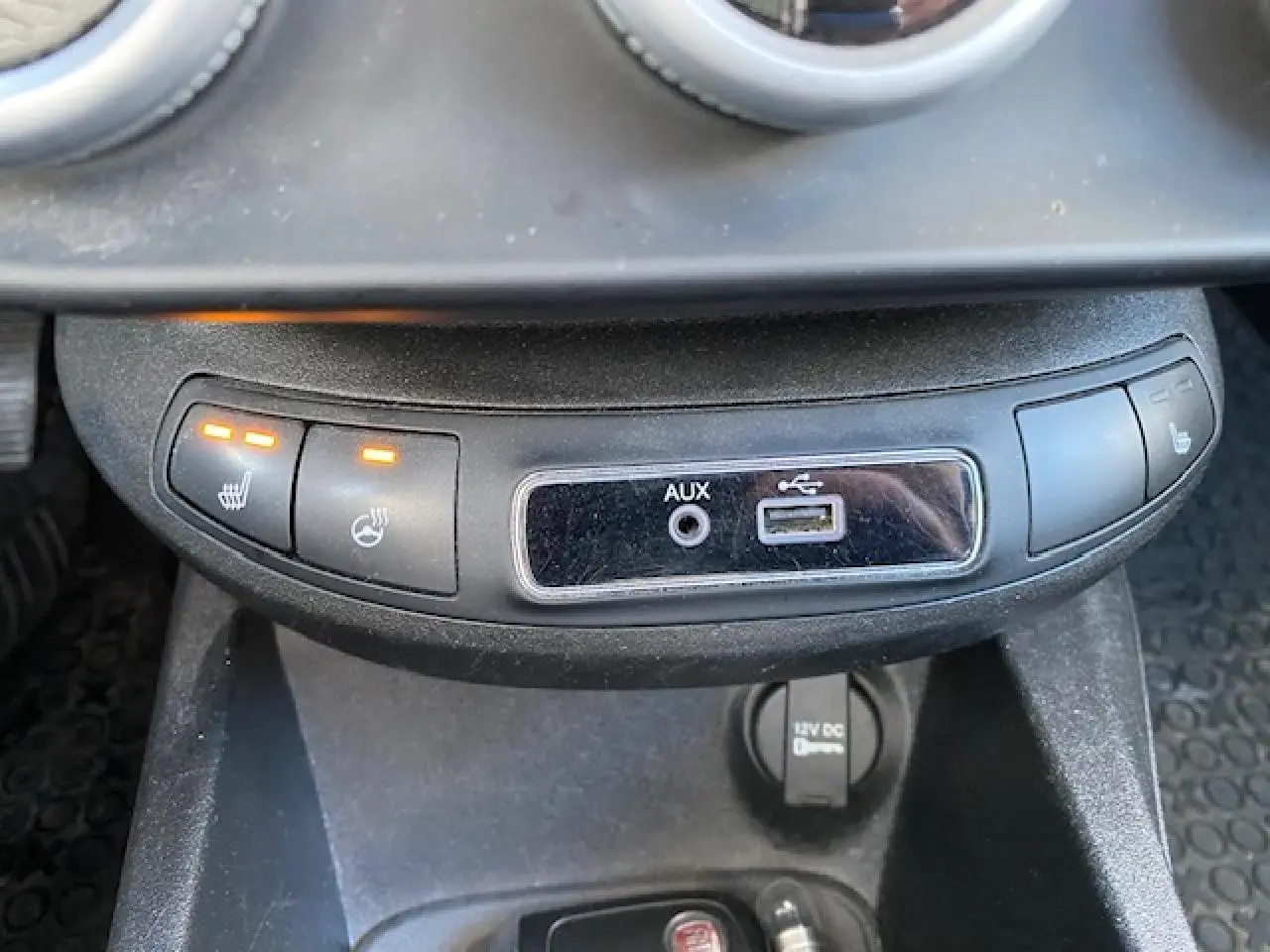 Vue rapprochée de la console centrale noire du Fiat 500X 2016, avec boutons de sièges chauffants et ports AUX et USB.