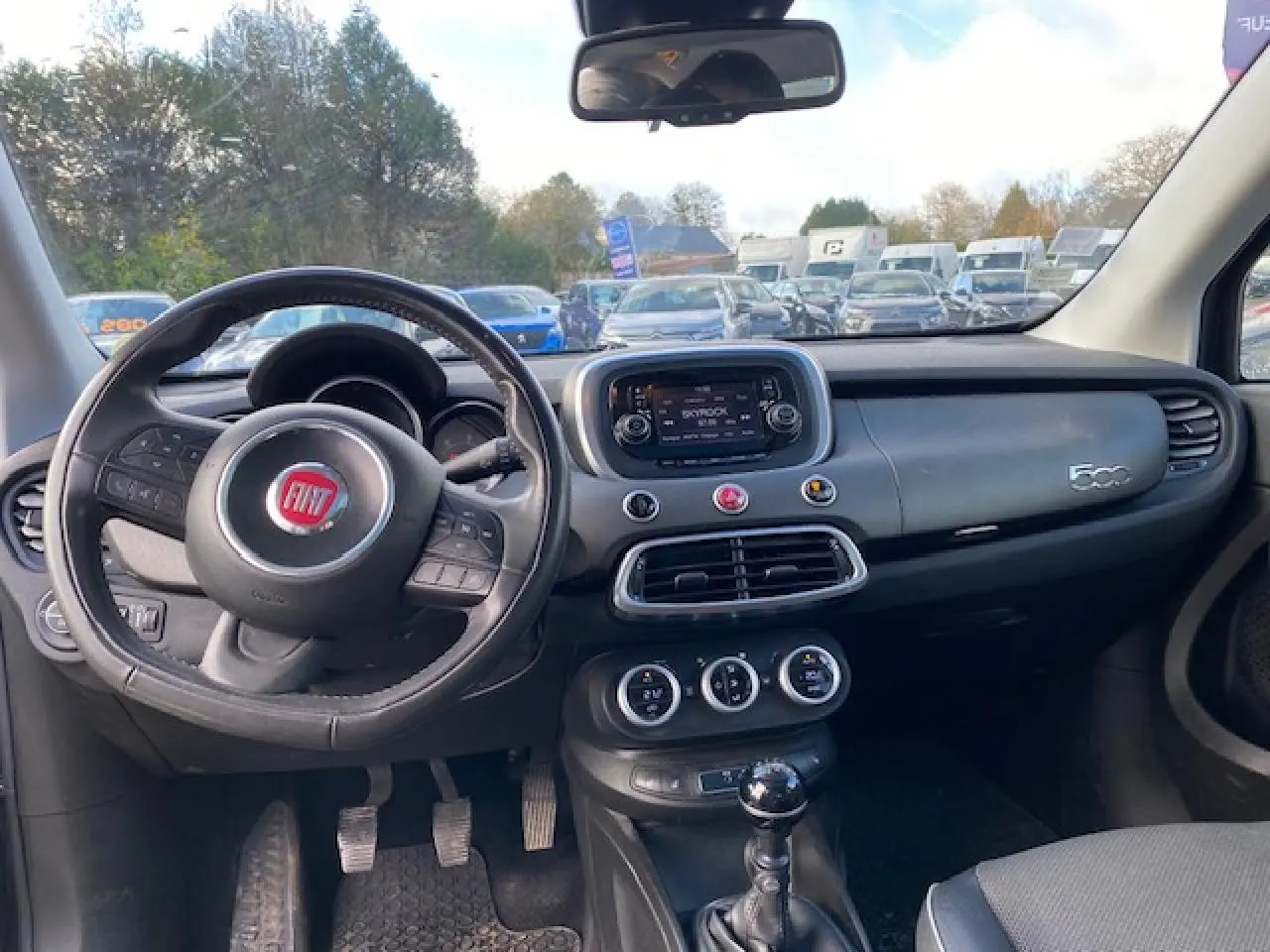 Intérieur de la Fiat 500X noir, vue du poste de conduite avec volant, tableau de bord et levier de vitesses manuelle visibles.