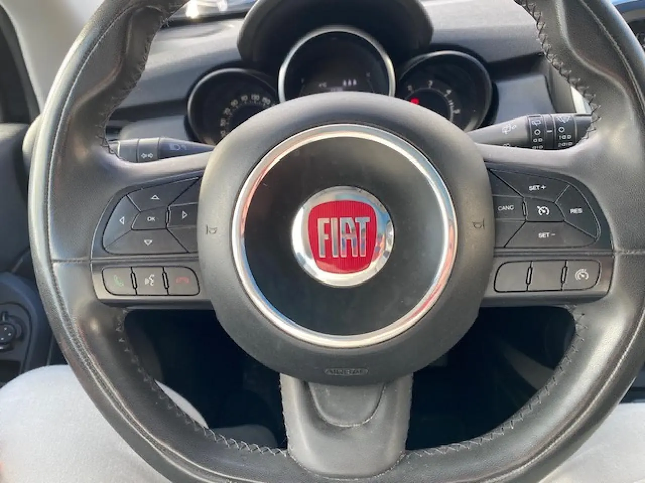 Vue rapprochée du volant noir de la Fiat 500X 2016 avec commandes intégrées et logo central rouge.