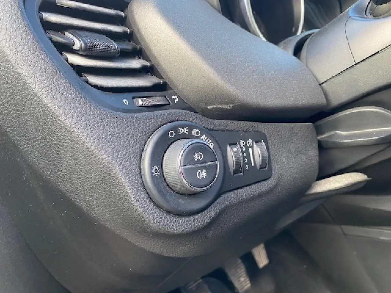 Gros plan sur la commande des phares et la ventilation côté gauche du tableau de bord noir d'une Fiat 500X Cross 2016.