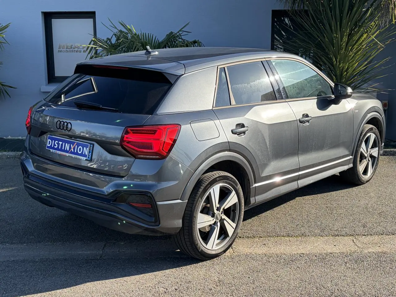 Audi Q2 gris Daytona en vue 3/4 arrière droit, avec jantes alliage 18 pouces et vitres arrière surteintées.