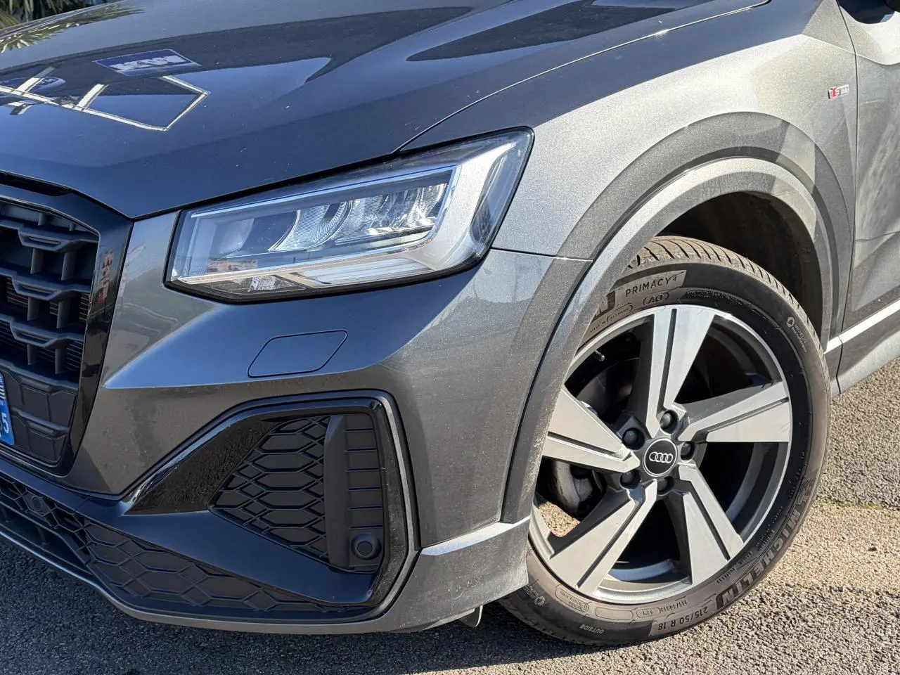 Gros plan sur l’avant droit de l’Audi Q2 gris Daytona 2024, mettant en valeur le phare LED et la jante alliage 18 pouces S line.