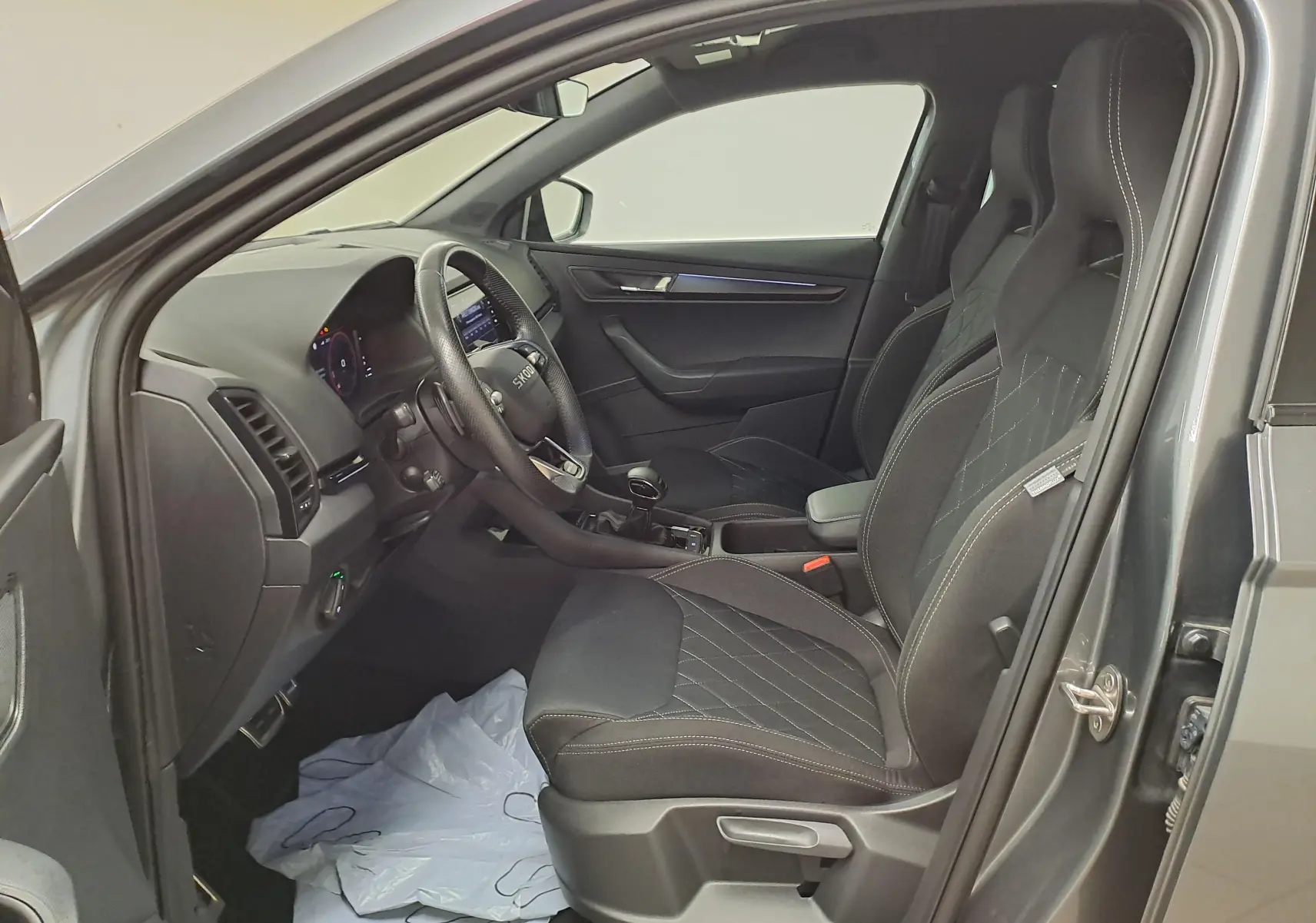 Vue intérieure côté conducteur du Skoda Karoq gris graphite 2025, sièges sport avec surpiqûres blanches et tableau de bord moderne.