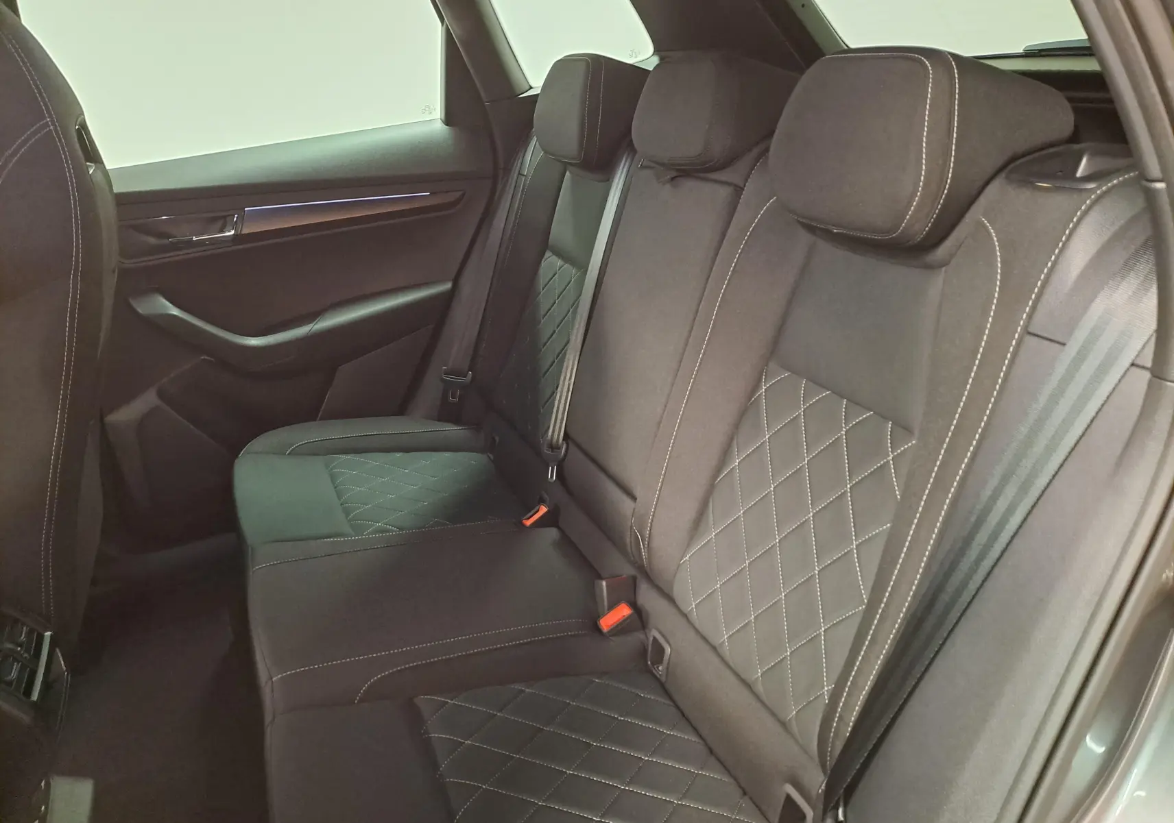 Vue intérieure côté arrière droit montrant les sièges arrière en tissu noir avec surpiqûres blanches du Skoda Karoq 2025.