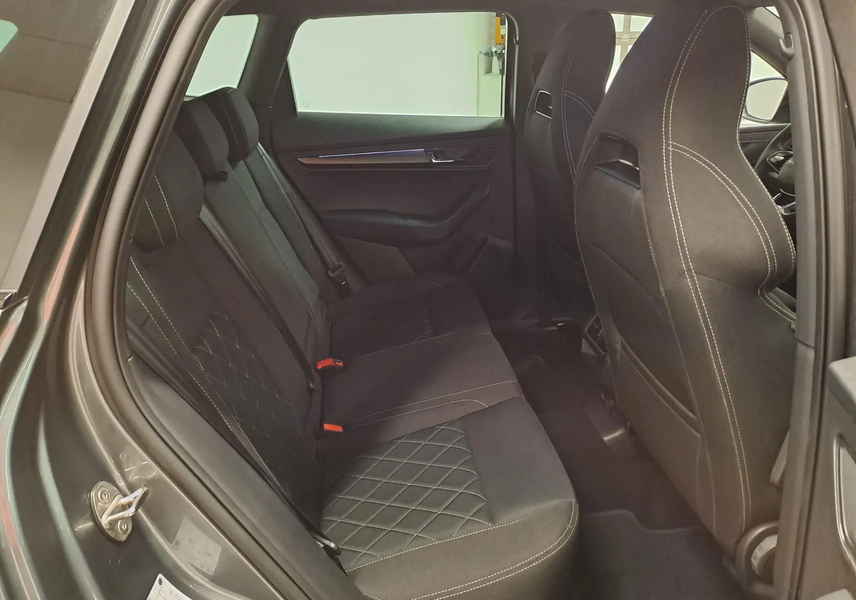 Vue intérieure côté gauche des sièges arrière noirs avec surpiqûres blanches du Skoda Karoq gris graphite 2025 Sportline.