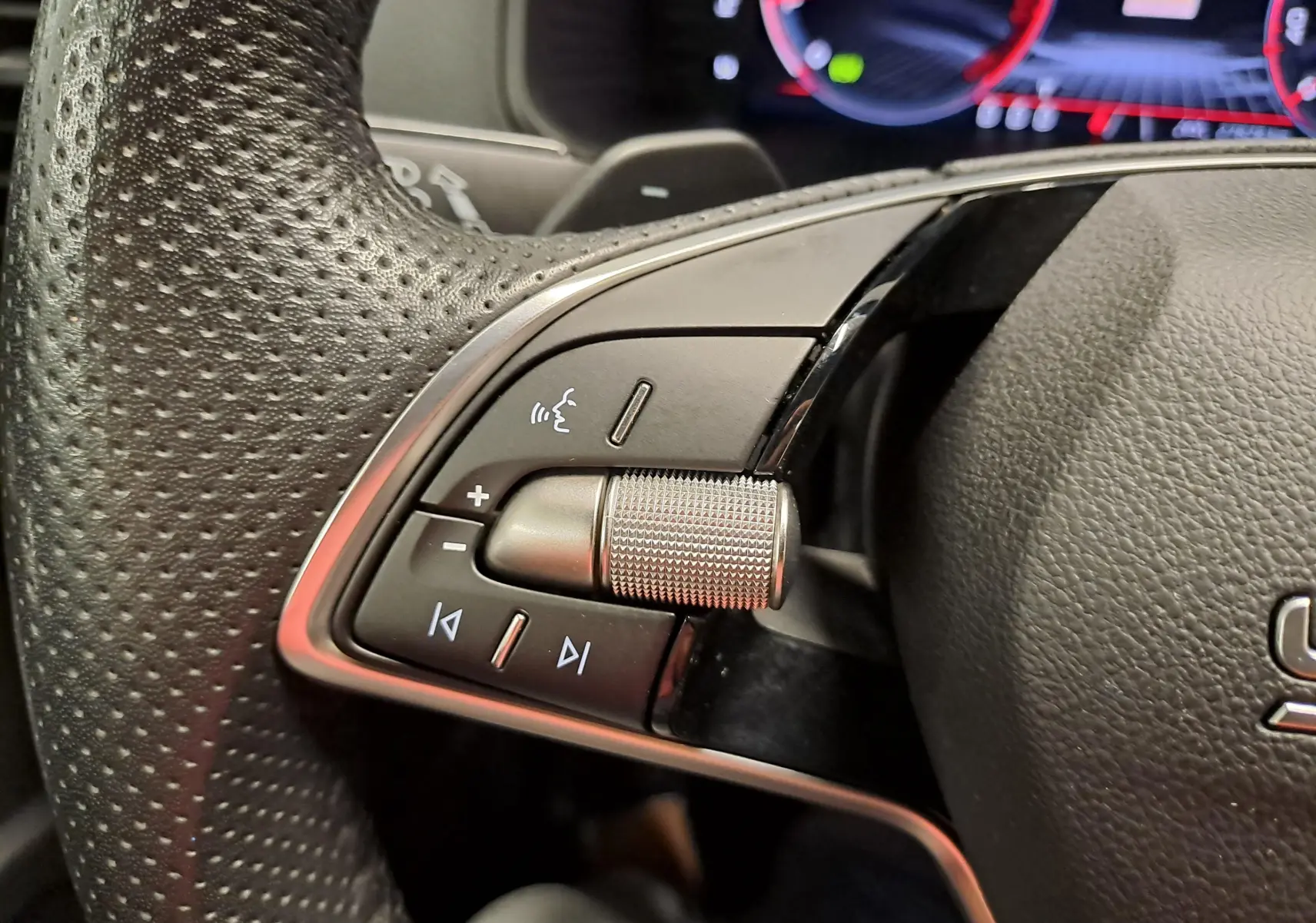 Gros plan sur les commandes gauche du volant perforé du Skoda Karoq 2025, avec molette et boutons multifonctions.