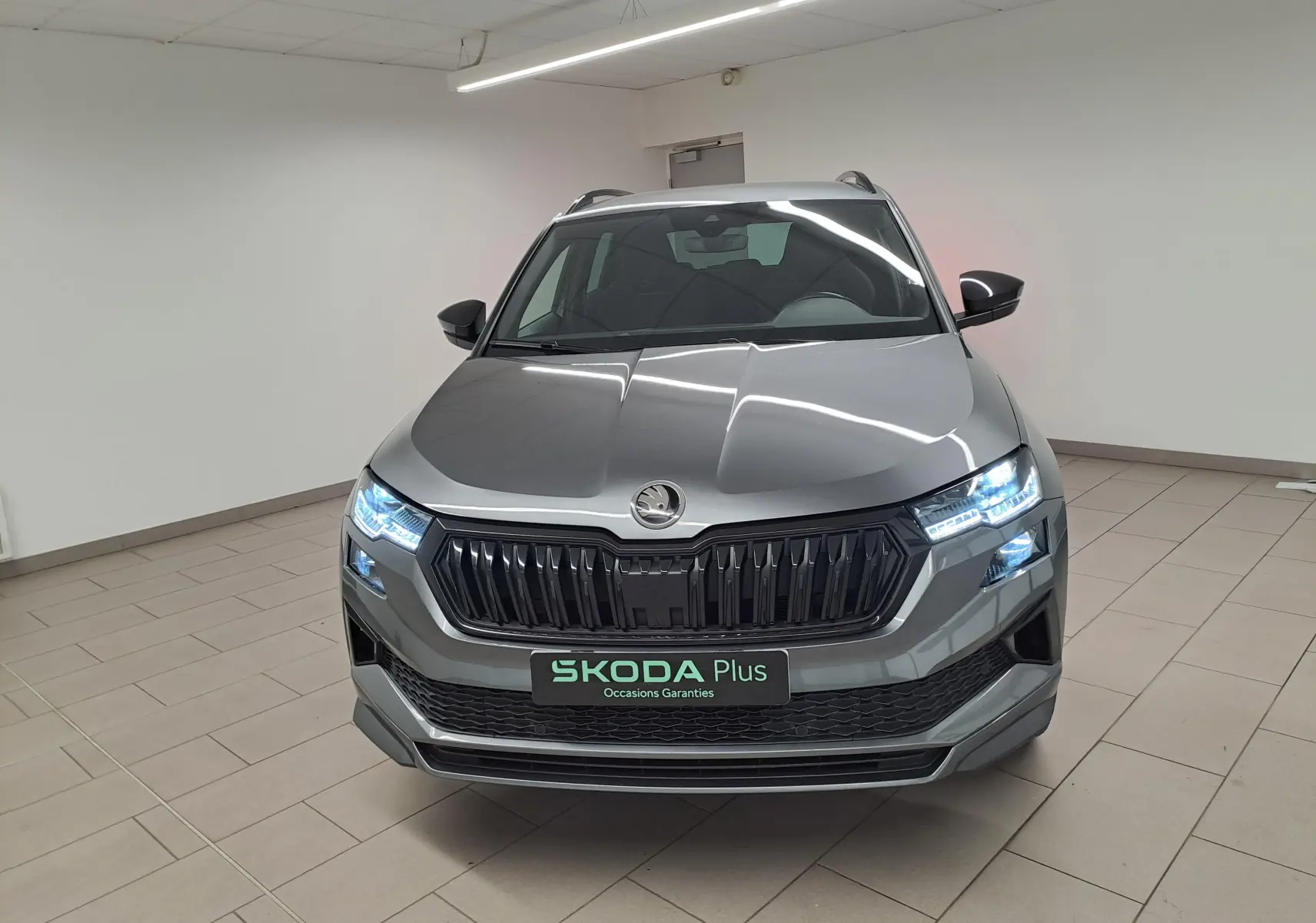 Vue frontale d'un Skoda Karoq gris graphite 2025 avec phares allumés et calandre noire sportive.