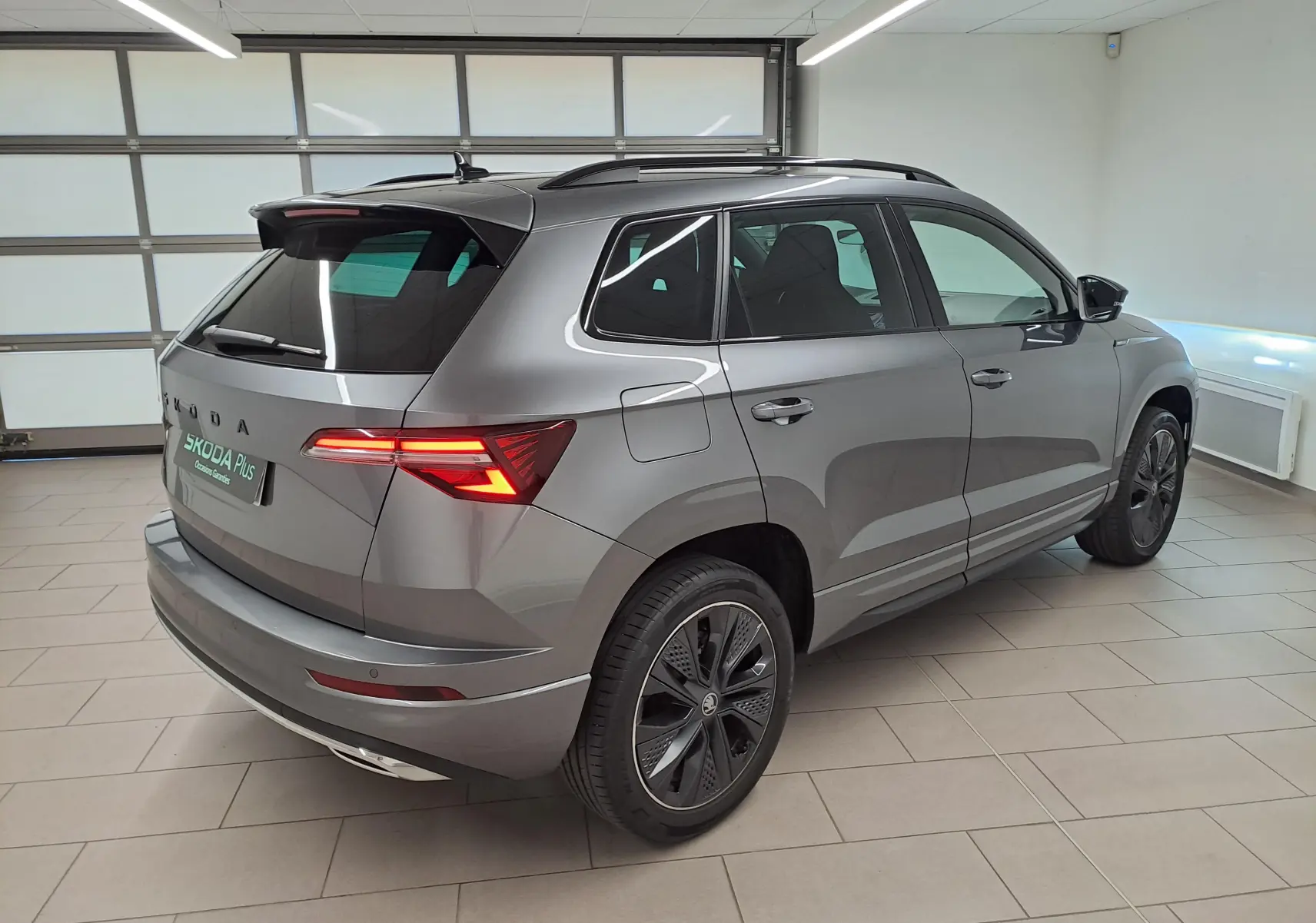 Vue 3/4 arrière droite du Skoda Karoq gris graphite métallisé avec feux allumés et jantes spécifiques Sportline.